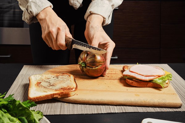 Close up view of hands of unrecognizable woman cutting tomato for sandwich