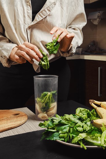 Hands of unrecognizable woman drop spinach into blender