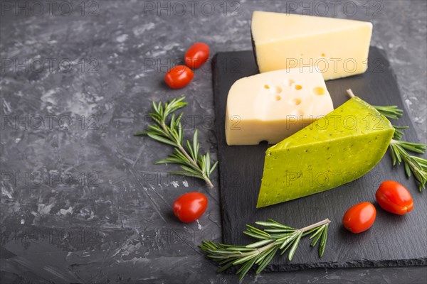 Green basil cheese and various types of cheese with rosemary and tomatoes on black slate board on a black concrete background. Side view, close up, copy space, selective focus