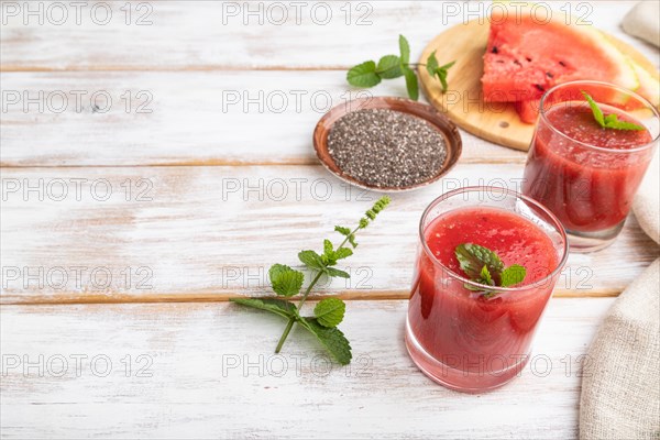 Watermelon juice with chia seeds and mint in glass on a white wooden background with linen textile. Healthy drink concept. Side view, copy space