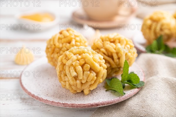 Traditional Tatar candy chak-chak made of dough and honey with cup of coffee on a white wooden background and linen textile. Side view, close up, selective focus