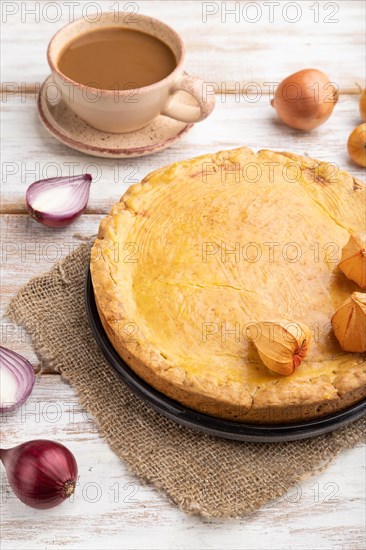 Autumn onion pie and cup of coffee on white wooden background and linen textile. Side view, close up