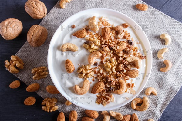 White plate with greek yogurt, granola, almond, cashew, walnuts on black wooden background. top view