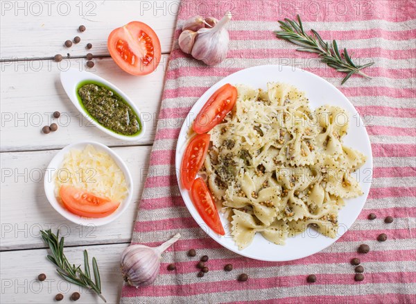 Farfalle pasta with pesto sauce, tomatoes and cheese on a linen tablecloth on white wooden background. top view, close up