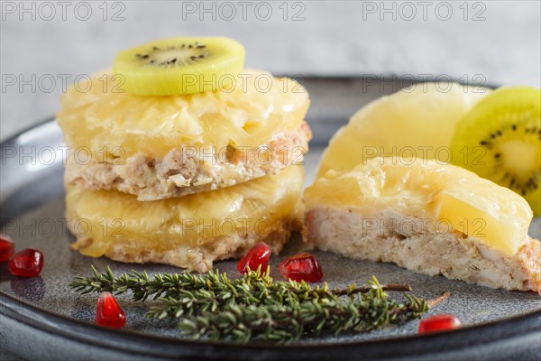 Pieces of baked pork with pineapple, cheese and kiwi on gray plate, side view, close up, selective focus