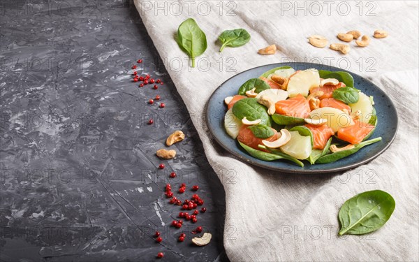 Fresh salmon with pineapple, spinach and cashew on a black concrete background. Side view, copy space, linen tablecloth
