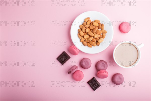 Purple and pink macaron or macaroon cakes with cup of coffee and almonds on pastel pink background. Morninig, spring, fashion composition. Flat lay, top view, copy space