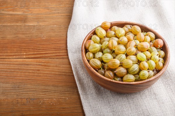 Fresh green gooseberry in wooden bowl on wooden background. side view, copy space