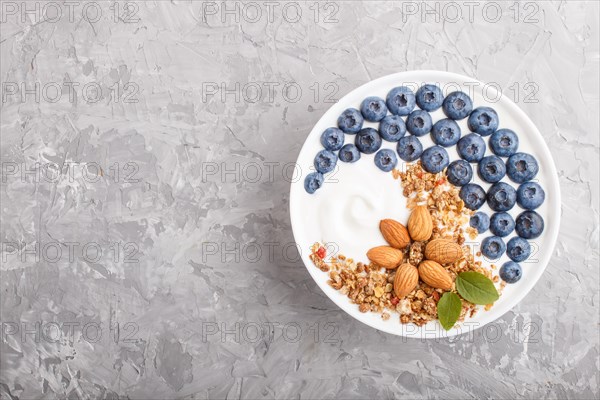 Yoghurt with blueberry, granola and almond in white plate on gray concrete background. top view, flat lay, copy space