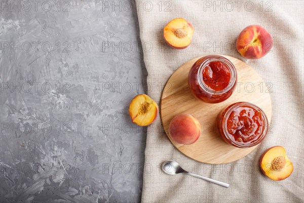 Peach jam in a glass jar with fresh fruits and linen textile on gray concrete background. top view, flat lay, copy space