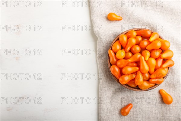 Fresh orange grape tomatoes in wooden bowl on white wooden background with linen napkin. top view, flat lay, copy space