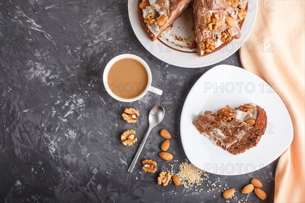 Homemade cake with milk cream, cocoa, almond, hazelnut on a black concrete background with orange textile and a cup of coffee. Top view, flat lay, copy space