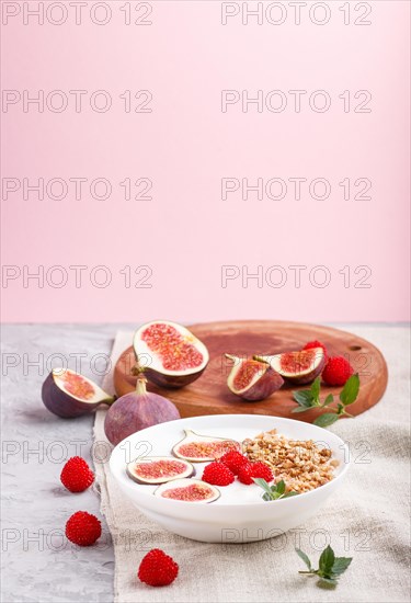 Yoghurt with raspberry, granola and figs in white plate on a gray and pink background and linen textile. side view, copy space