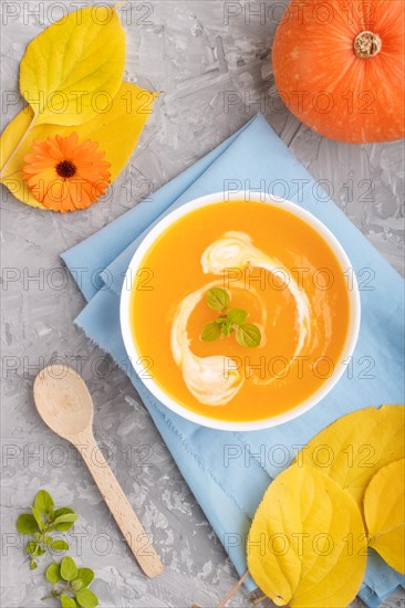 Traditional pumpkin cream soup with in white bowl on a gray concrete background with blue napkin. top view, flat lay, close up