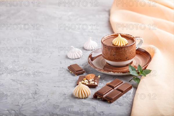 Cup of hot chocolate and pieces of milk chocolate with almonds on a gray concrete background with orange textile. side view, copy space