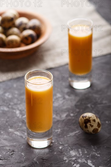 Sweet egg liqueur in glass with quail eggs on a black concrete background. Side view, low key, close up