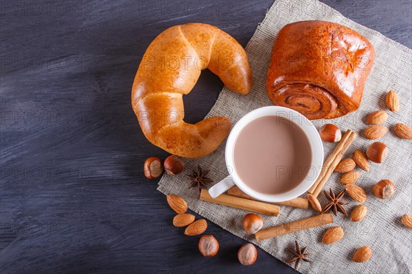 A cup of hot chocolate with nuts, buns and spices on linen napkin and black wooden background. copy space, top view