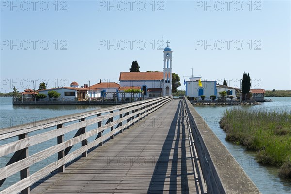 A wooden footbridge leads over calm waters to a monastery under a clear blue sky, Monastery of St Nicholas, Monastery of Agios Nikolaos, Agiou Nikolaou, Vistonidas Burma Lagoon, Porto Lagos, Xanthi, Eastern Macedonia and Thrace, Greece, Europe