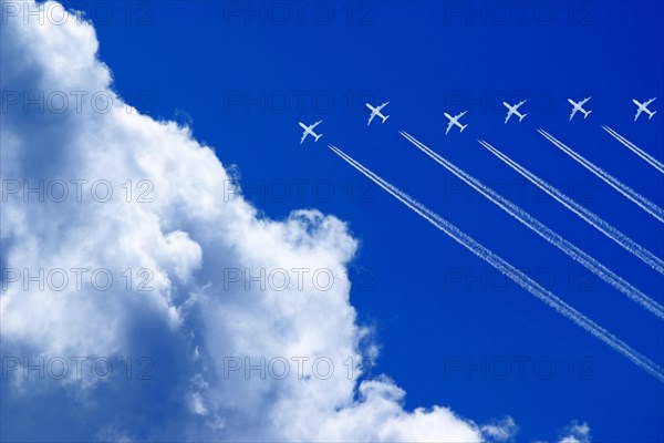 Seven aeroplanes with contrails flying high in the blue sky in formation