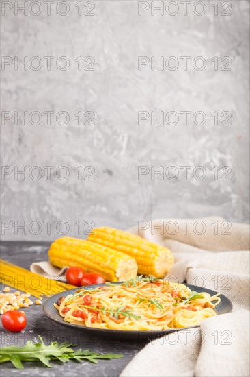 Corn noodles with tomato sauce and arugula on a black concrete background and linen textile. Side view, copy space