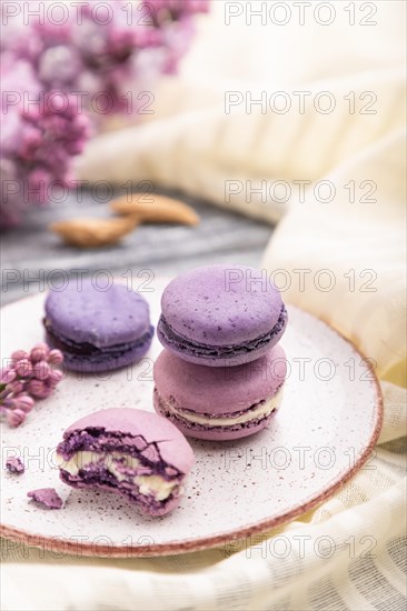 Purple macarons or macaroons cakes with cup of coffee on a gray wooden background and white linen textile. Side view, close up, selective focus
