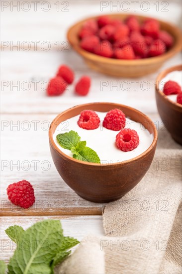 Yogurt with raspberry in clay cups on white wooden background and linen textile. Side view, close up, selective focus