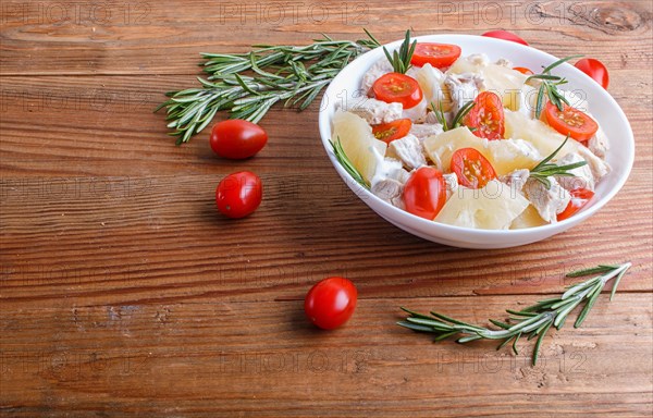 Chicken fillet salad with rosemary, pineapple and cherry tomatoes on brown wooden background. close up, copy space