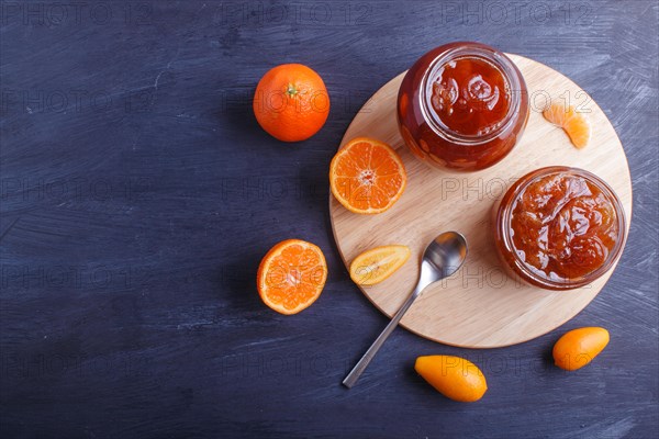 Tangerine and kumquat jam in a glass jar with fresh fruits on a black wooden table. Homemade, copy space, top view