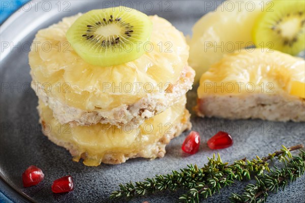 Pieces of baked pork with pineapple, cheese and kiwi on gray plate and blue background, side view, close up, selective focus