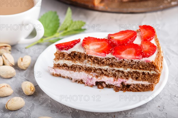 Homemade cake with yoghurt cream, strawberry, pistachio and a cup of coffee on a gray concrete background. side view, selective focus, close up