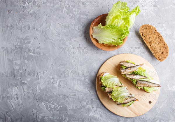Sprats sandwiches with lettuce and cream cheese on wooden board on a gray concrete background. top view, copy space, flat lay