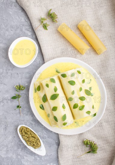 Cannelloni pasta with egg sauce, cream cheese and oregano leaves on a gray concrete background with linen textile. top view, flat lay, close up