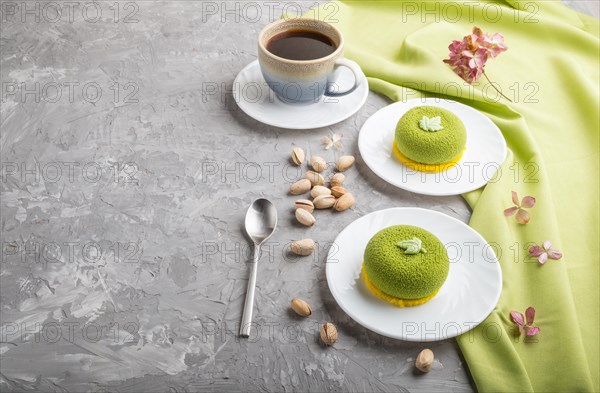 Green mousse cake with pistachio cream and a cup of coffee on a gray concrete background and green textile. side view, copy space