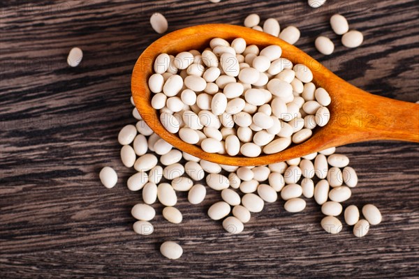 Pile of white beans in a wooden spoon isolated on a gray wooden background. Top view