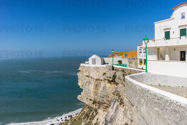 White buildings on steep cliffs overlook a calm sea under a clear blue sky Nazareh Portugal