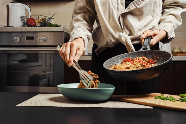 Unrecognizable woman moving cooked noodles with vegetables and beef from frying pan into plate