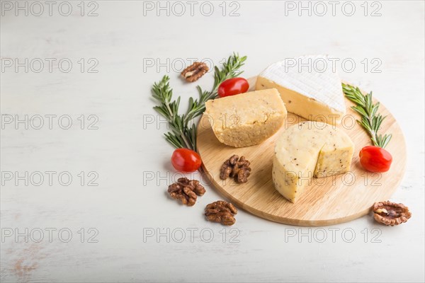 Cheddar and various types of cheese with rosemary and tomatoes on wooden board on a white wooden background. Side view, copy space, selective focus