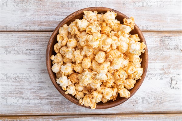 Popcorn with caramel in wooden bowl on a white wooden background. Top view, flat lay, close up