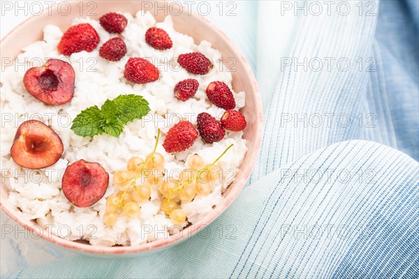 Rice flakes porridge with milk and strawberry in ceramic bowl on white concrete background and blue linen textile. Top view, flat lay, close up