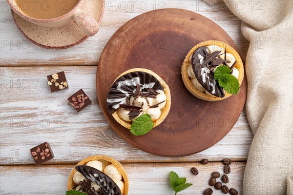 Sweet tartlets with chocolate and cheese cream with cup of coffee on a white wooden background and linen textile. top view, flat lay, close up