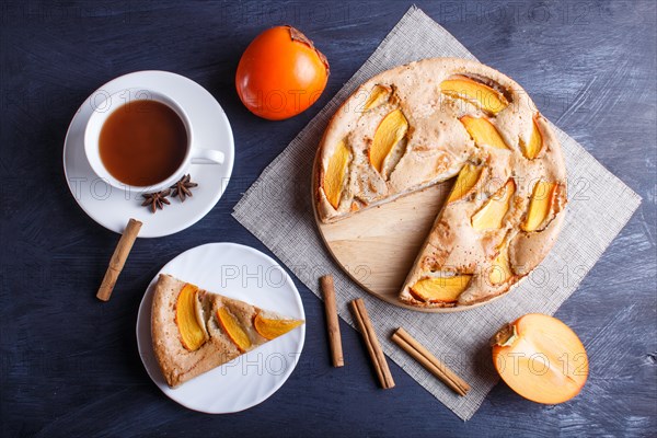 Sweet persimmon pie with cup of cocoa on black wooden background. top view