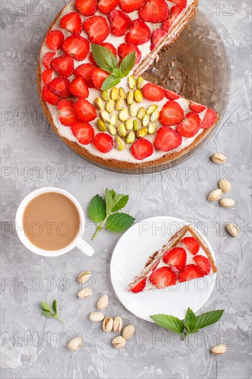 Homemade cake with yoghurt cream, strawberry, pistachio and a cup of coffee on a gray concrete background. top view. flat lay, close up