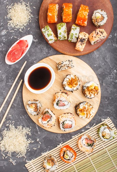 Different kinds of maki sushi rolls with salmon, sesame, cheese, roe and chopsticks, soy sauce, marinated ginger on a black concrete background. Top view, flat lay, close up. Japanese food concept