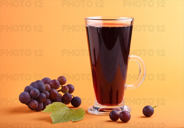 Glass of red grape juice on orange background. Morninig, spring, healthy drink concept. Side view, close up