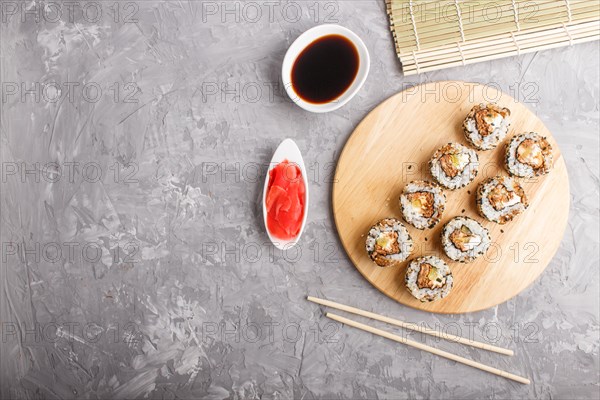 Japanese maki sushi rolls with salmon, sesame, cucumber chopsticks, soy sauce and marinated ginger on wooden board on a gray concrete background. Top view, copy space, flat lay