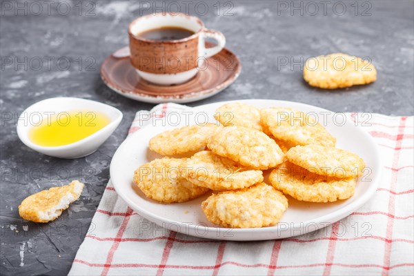 Traditional japanese rice chips cookies with honey and soy sauce on a white ceramic plate and a cup of coffee on a black concrete background. side view, close up, selective focus