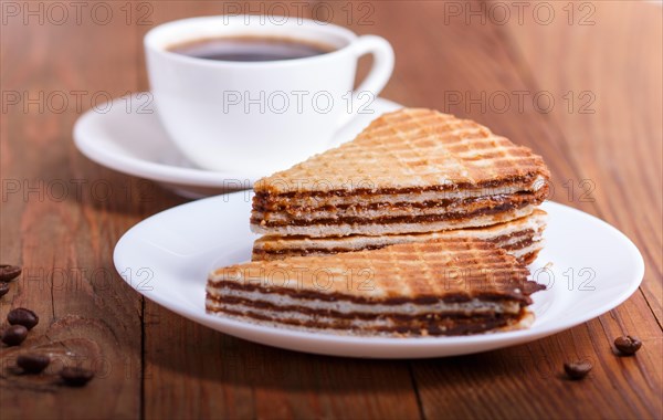 Waffle sandwiches with boiled condensed milk in plate on brown wooden table with cup of coffee. closeup