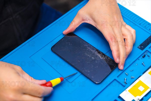 Close-up top view of a male technician uses a screwdriver to open the screen of a mobile phone in a repair shop