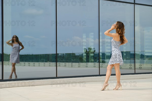 Woman posing in front of glass wall of a building looking at her reflection