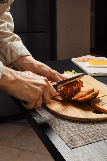 Close up side view of hands of unrecognizable woman cutting tomato for sandwich